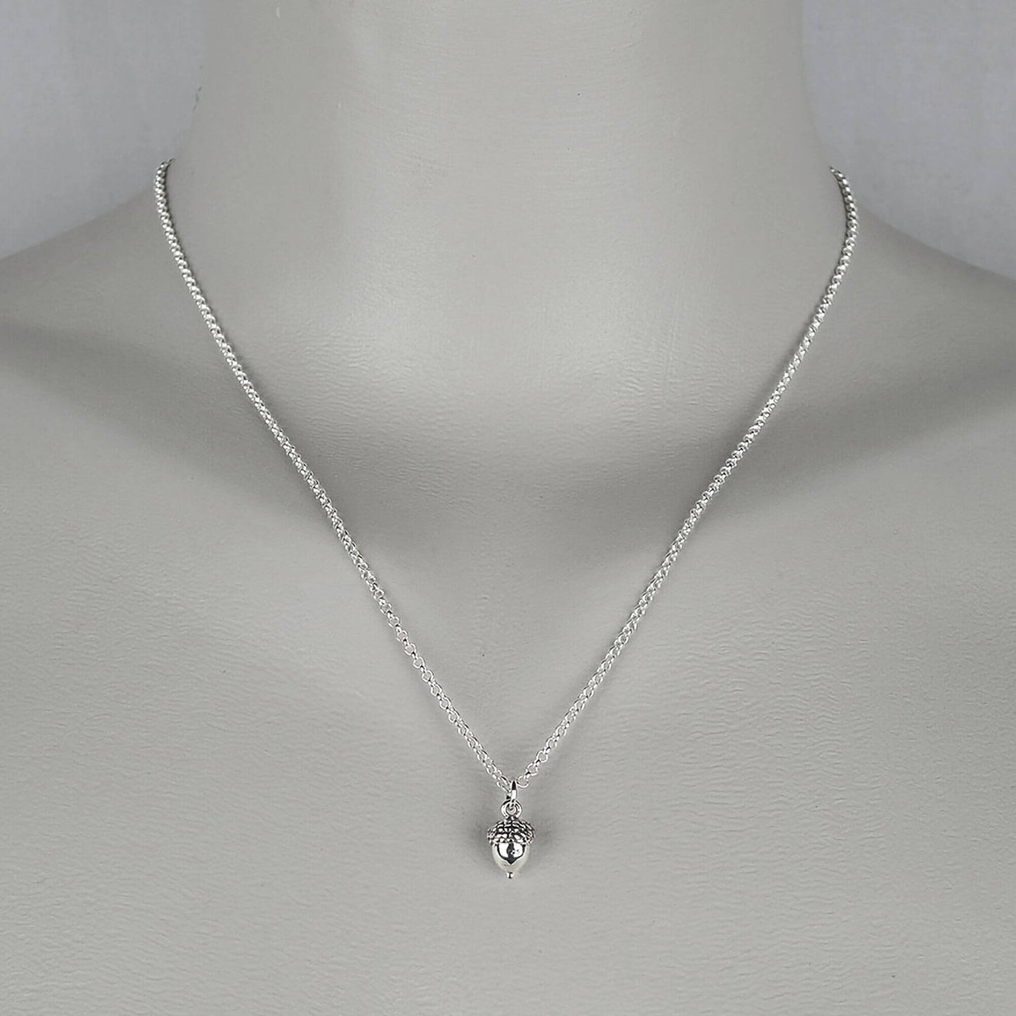A woman wearing a sterling silver chain necklace with a trendy petite small acorn charm.