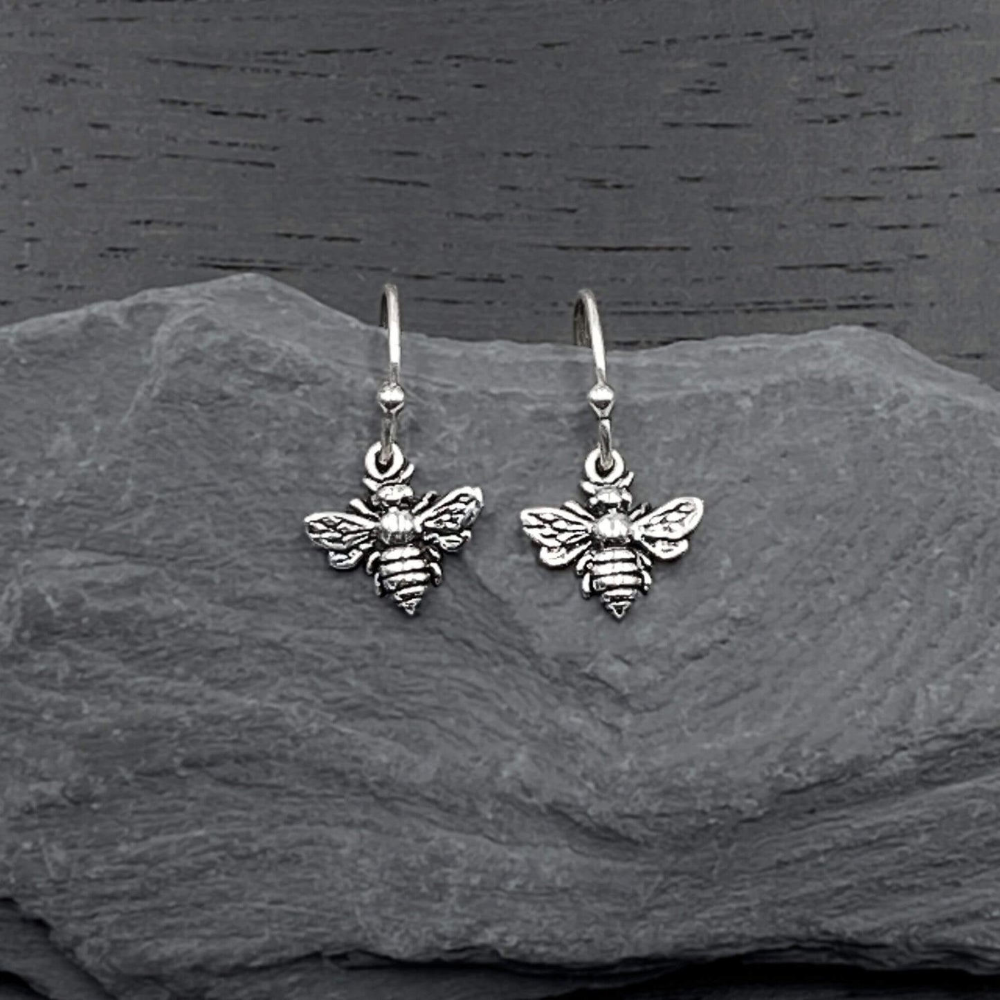 Detailed view of silver dangling earrings with a intricate bee design.