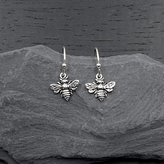 Detailed view of silver dangling earrings with a intricate bee design.