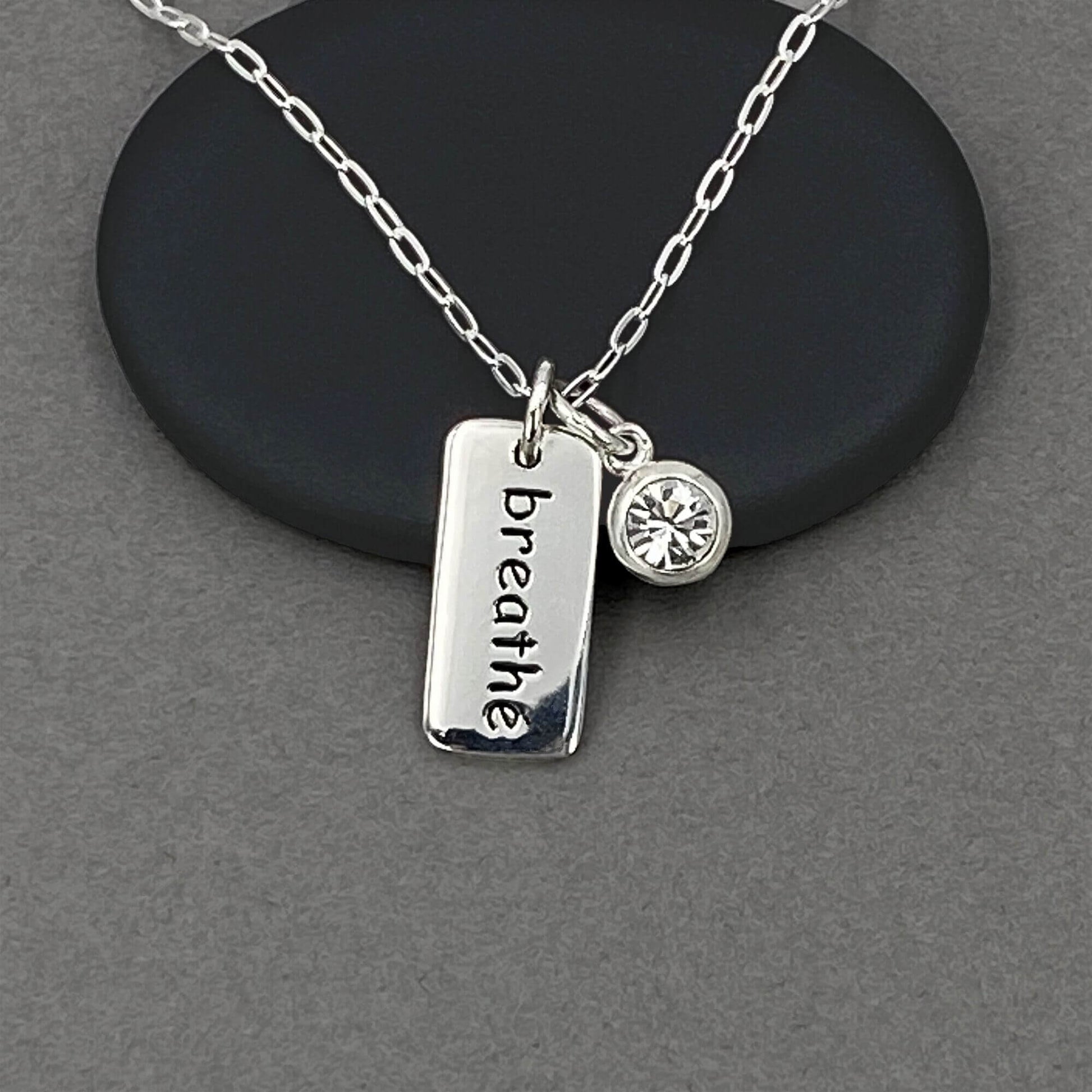 Detailed view of a tiny breathe word charm and a clear crystal diamond charm dangling.