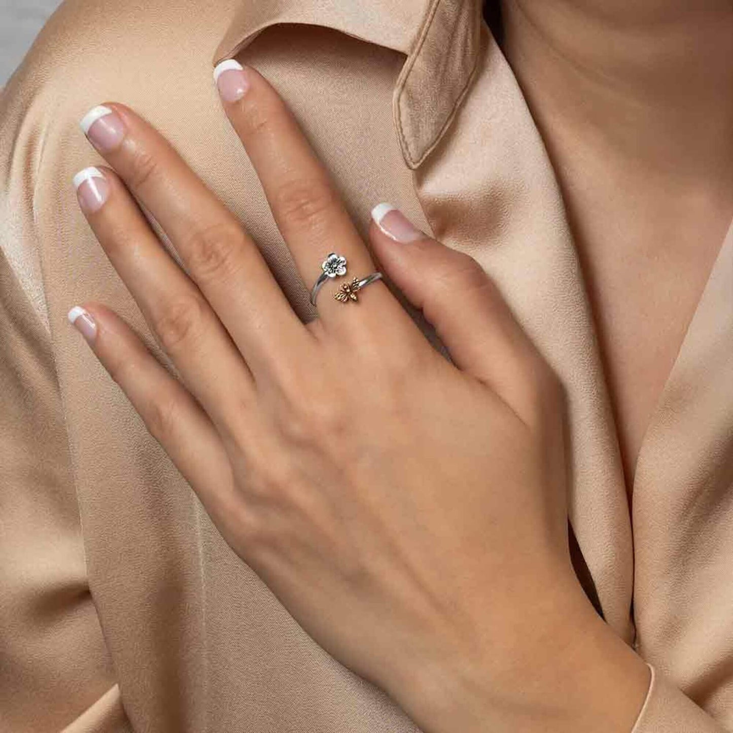 A woman's hand model wearing our petite sterling silver adjustable ring with a gold bee. The silver band wraps around the finger with the flower and bee aligning opposite each other with an open end.