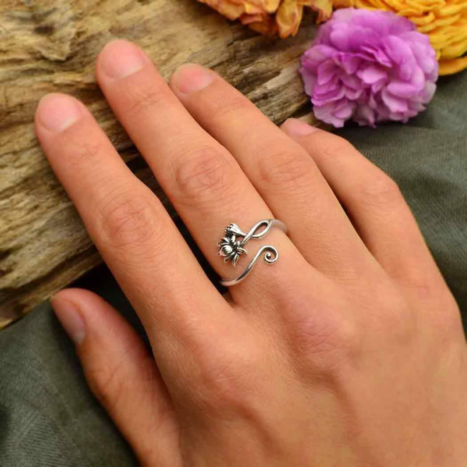 CLose up of a womans hand wearing a dainty lotus flower ring in shiny sterling silver with a swirl.