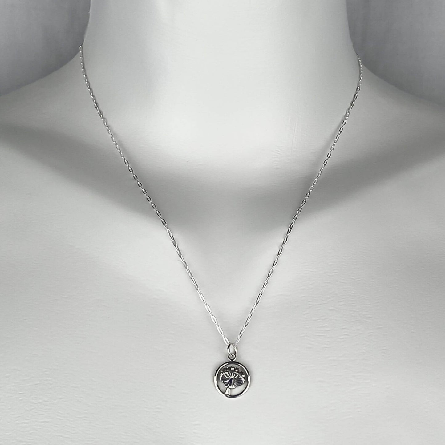 A woman wearing a sterling silver chain necklace with a trendy tiny mushroom on a round pendant small charm.