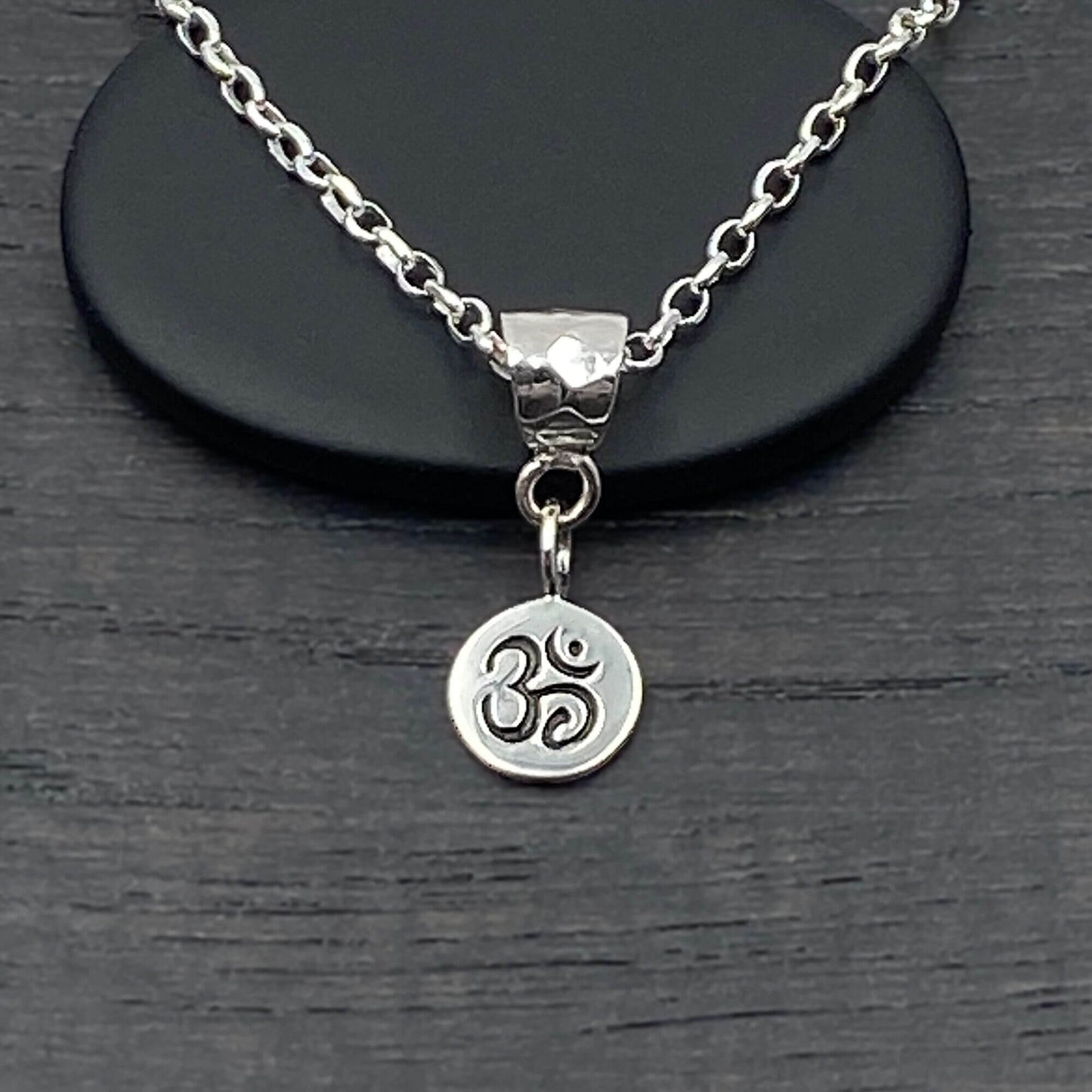 Detailed view of a handmade small Ohm Om charm that is etched with the Om symbol in a darker patina.