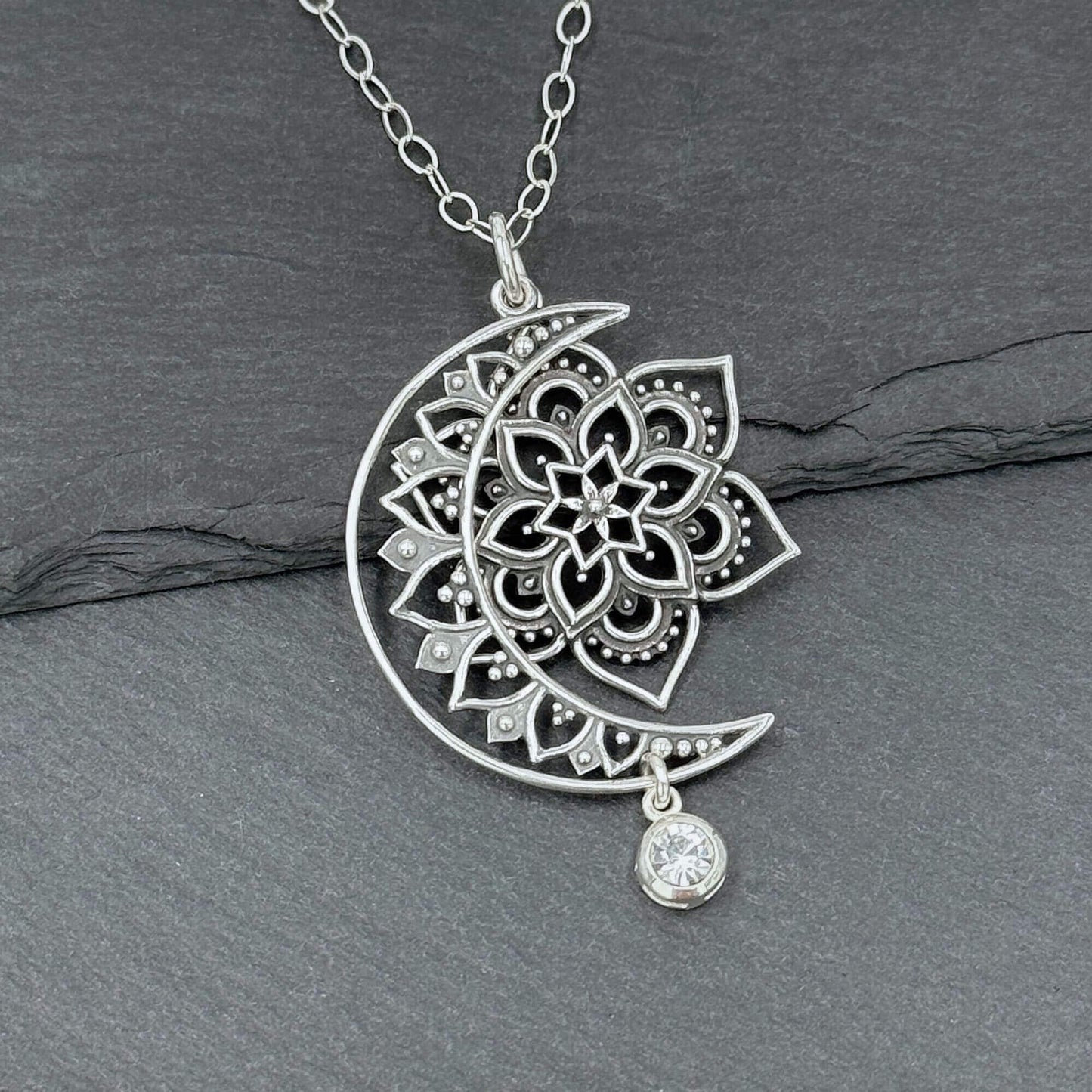 CLose up view of a 925 sterling silver sun, moon and star pendant necklace for women. The crescent moon and sun are cut out with intricate filigree shapes in the bali style. There is a crystal dangle hanging off the bottom of the moon.