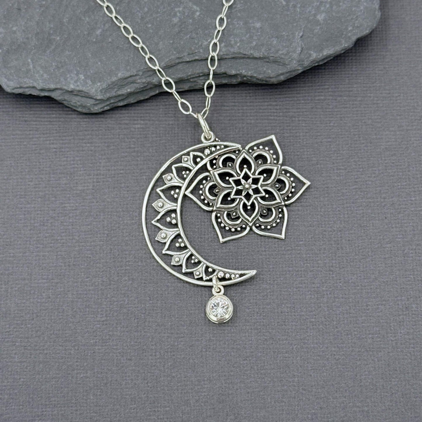 CLose up of sterling silver moon, sun and star pendant showing they dangle independently of each other. The pendant is on a sterling silver cable chain.