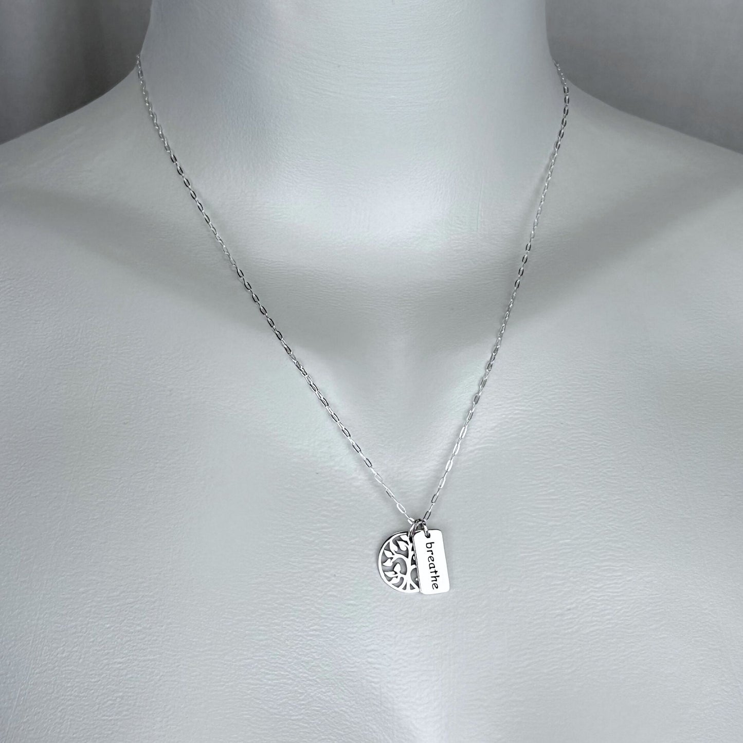 A woman wearing a 925 solid sterling silver necklace with a double charm of a tree and a breathe word pendant with a 925 solid sterling silver chain. Our silver jewelry collection is intended for females.