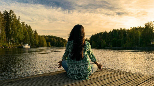 Woman meditating by a river in a forest for wellness.