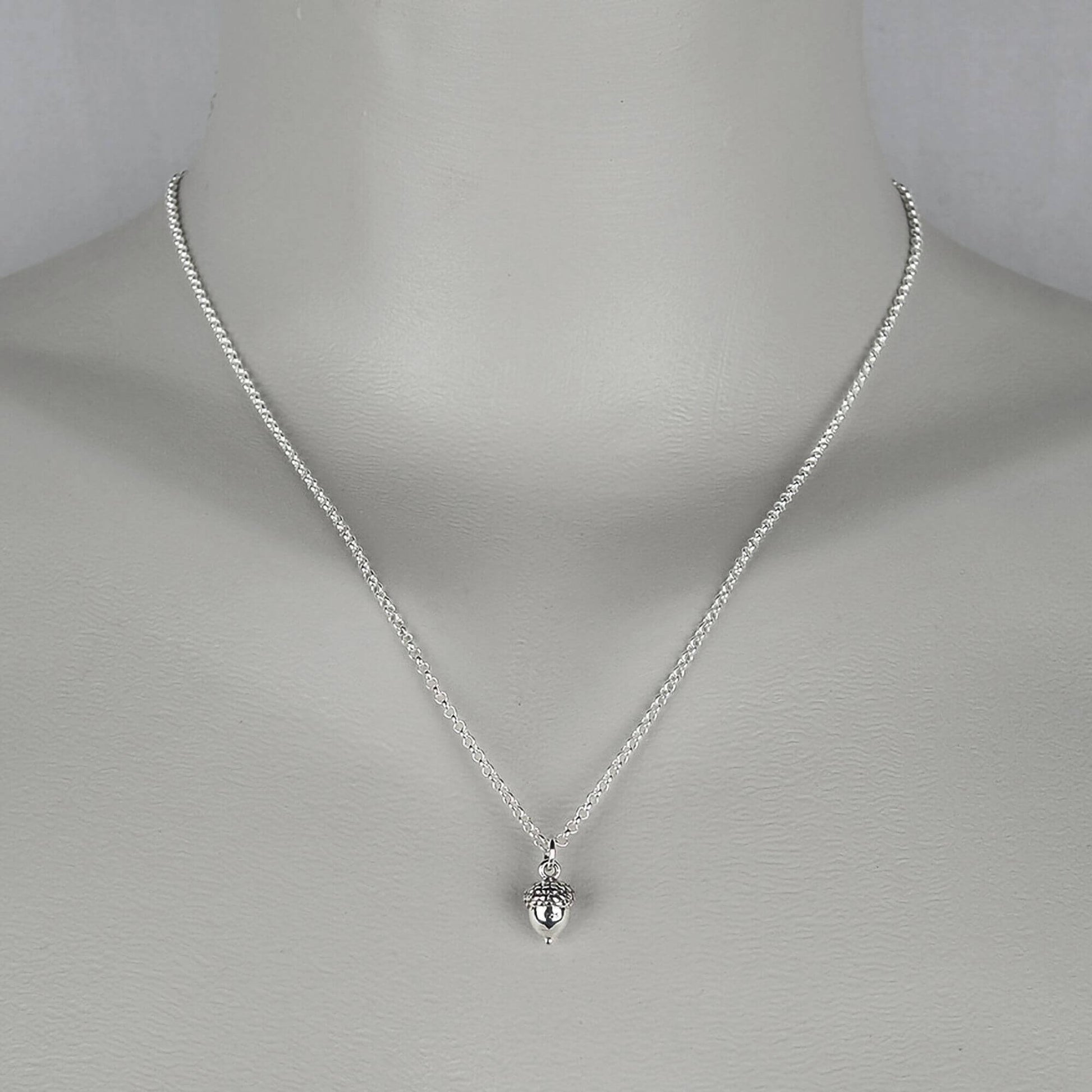 A woman wearing a sterling silver chain necklace with a trendy petite  small acorn charm.