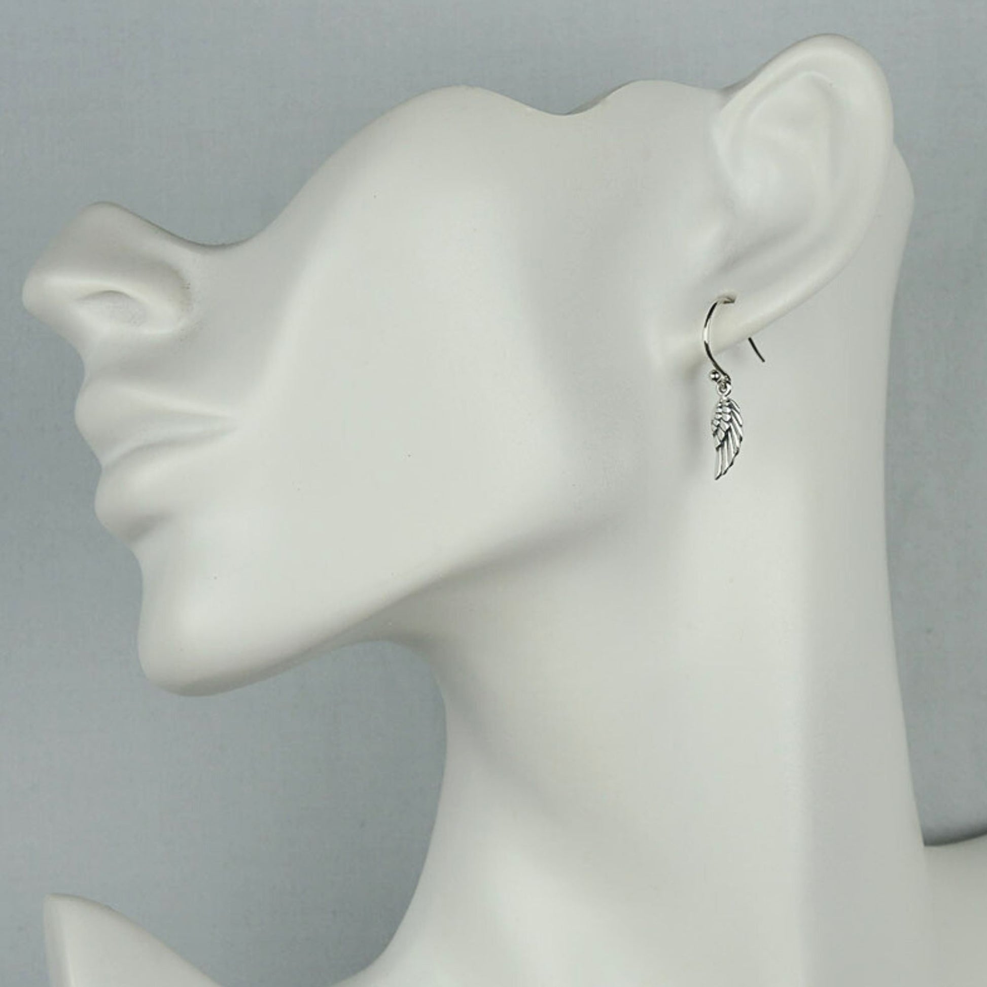 Model of a woman wearing small silver angel wing dangle earrings.