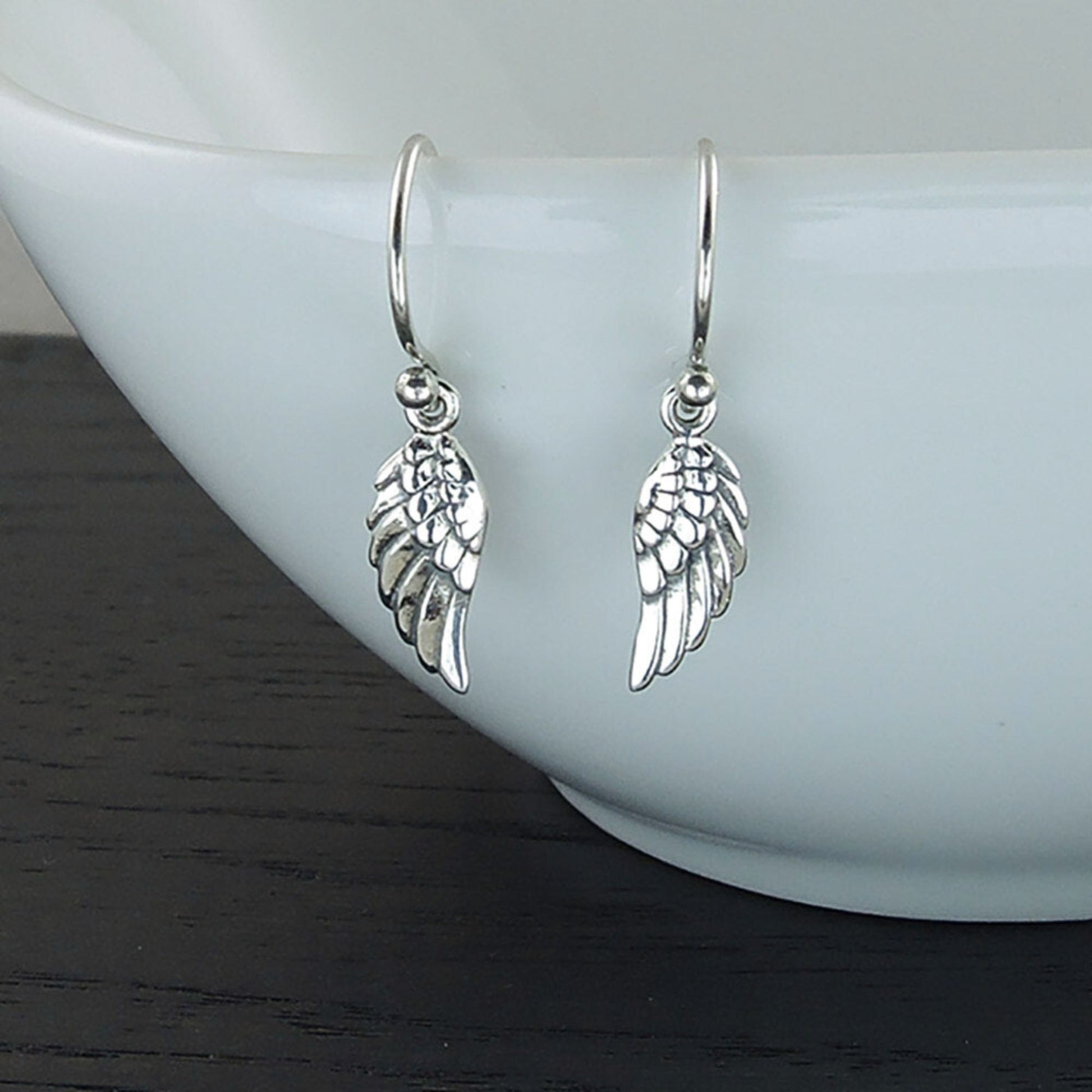 Detailed view of small silver earrings with a spiritually-inspired angel wing design.