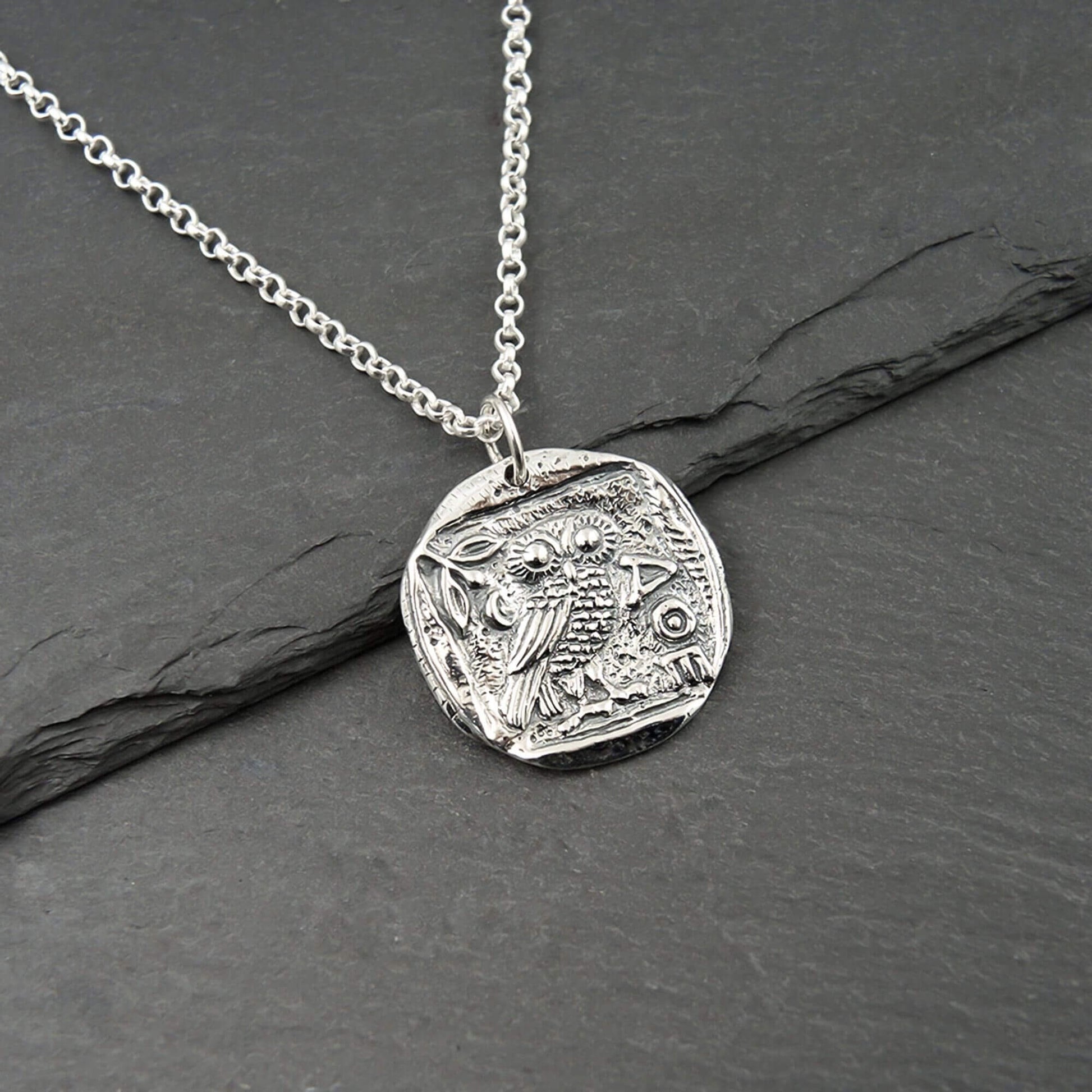 Close-up of a round coin-shaped silver AOE Athena owl pendant on a chain.