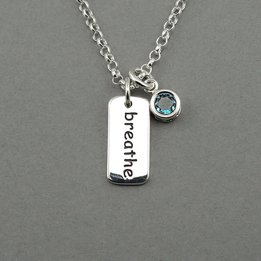 Rectangle shaped silver breathe word accented with a blue crystal dangle charm on a sterling silver chain.