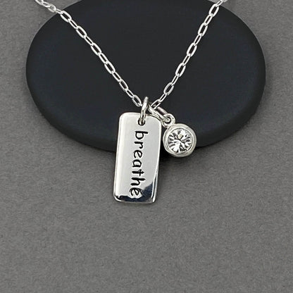 Detailed view of a tiny breathe word charm and a clear crystal diamond charm dangling. 