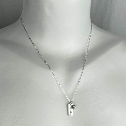 A woman wearing a sterling silver chain necklace with a yoga breathe word  small charm accented with a clear crystal dangle charm.