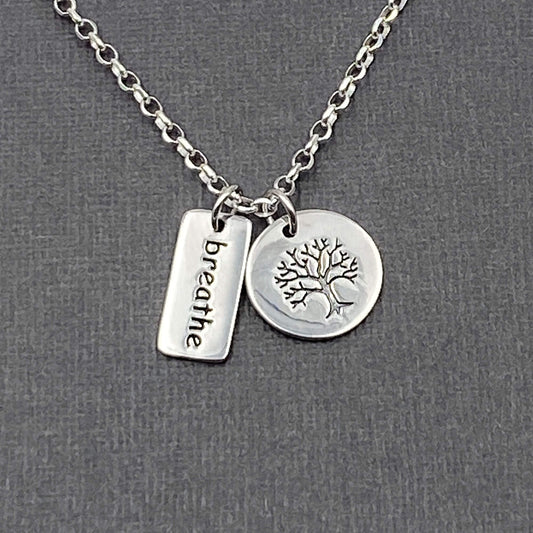 Two small etched tree and breathe word charm dangling independently on a sterling silver chain.