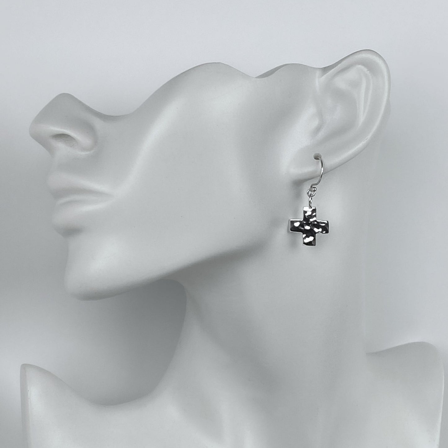 Model of a woman wearing minimalistic silver hammered cross dangle earrings.