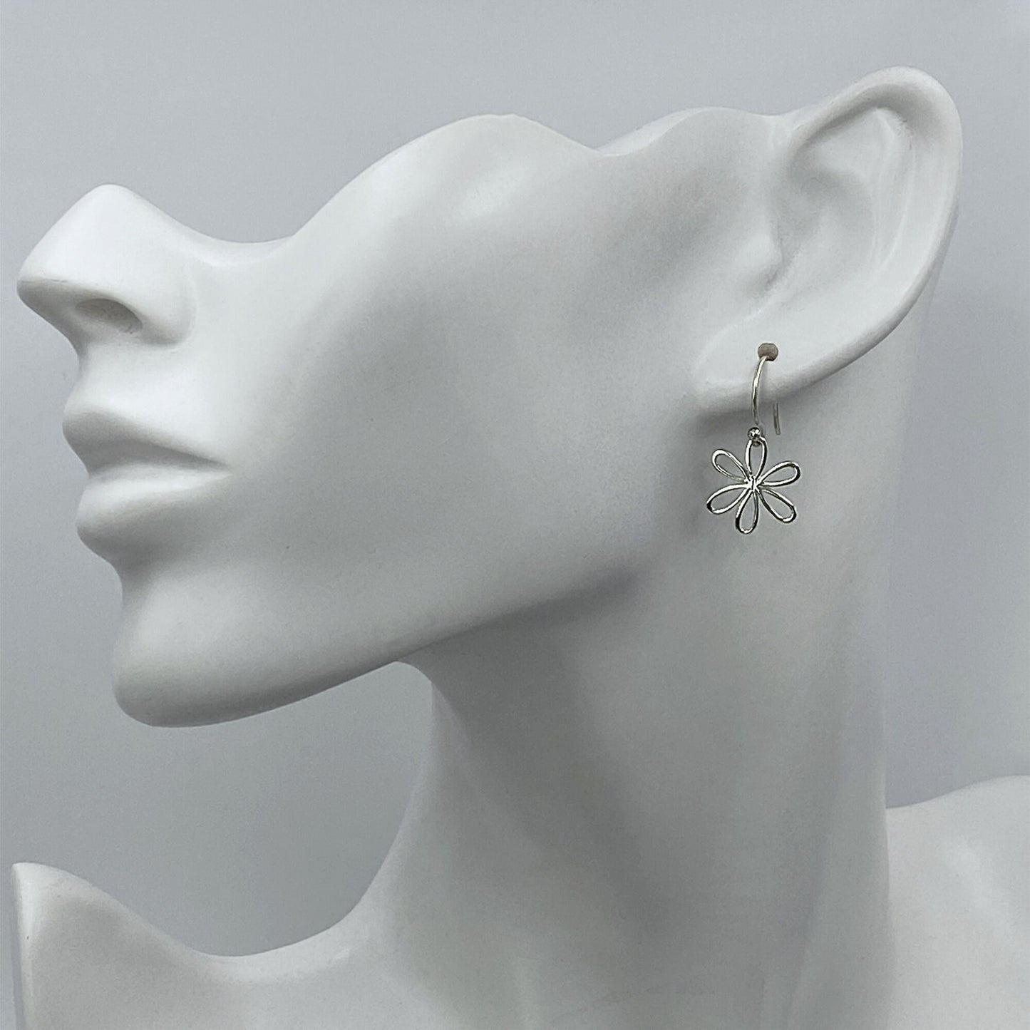 Model of a woman wearing small sterling silver daisy dangle earrings.