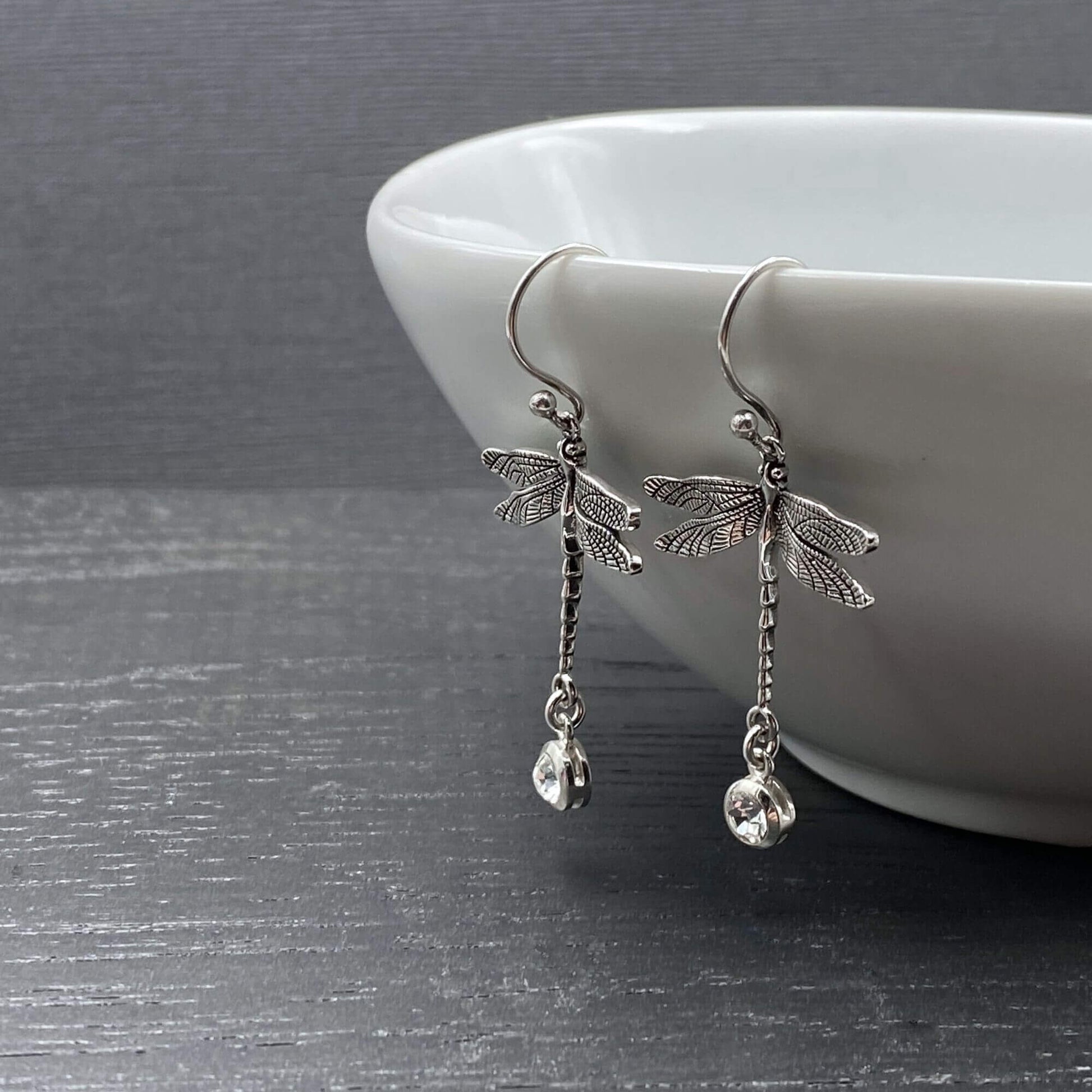 Sterling silver dangle earrings on silver hook ear wires with a n intricate dragonfly design and additional dangling crystal.