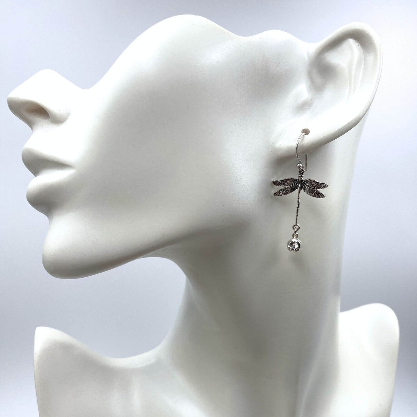 Model of a woman wearing elegant, detailed silver dragonfly dangle earrings.