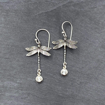 Detailed view of silver feminine earrings with a nature-inspired dragonfly design and dangling crystal.