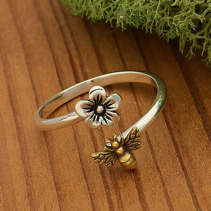 Close up of a sterling silver adjustable band ring with a sterling flower on one open end and a gold bronze bee on the other. 