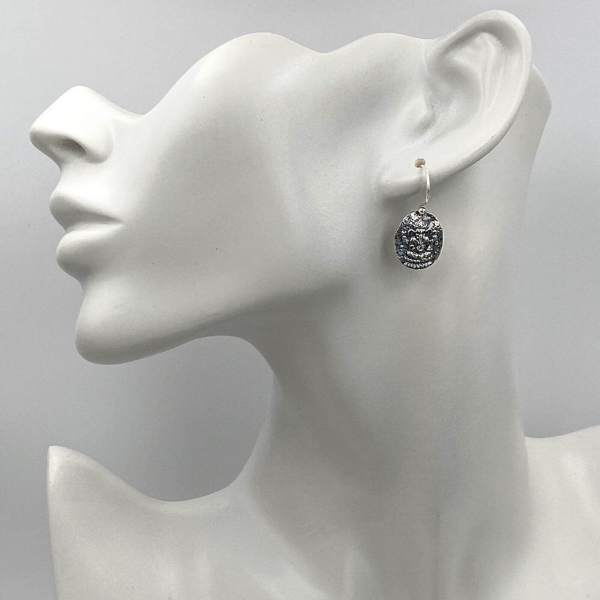 Model of a woman wearing small, intricate silver Ganesh dangle earrings.