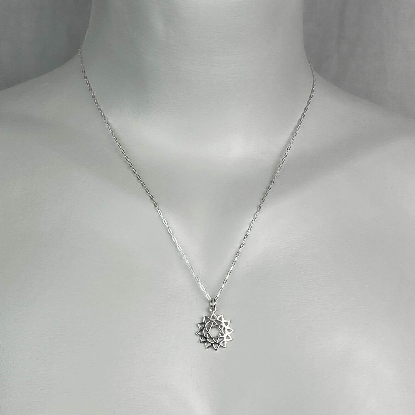 A woman model wearing a sterling silver chain necklace with a small silver heart chakra charm.