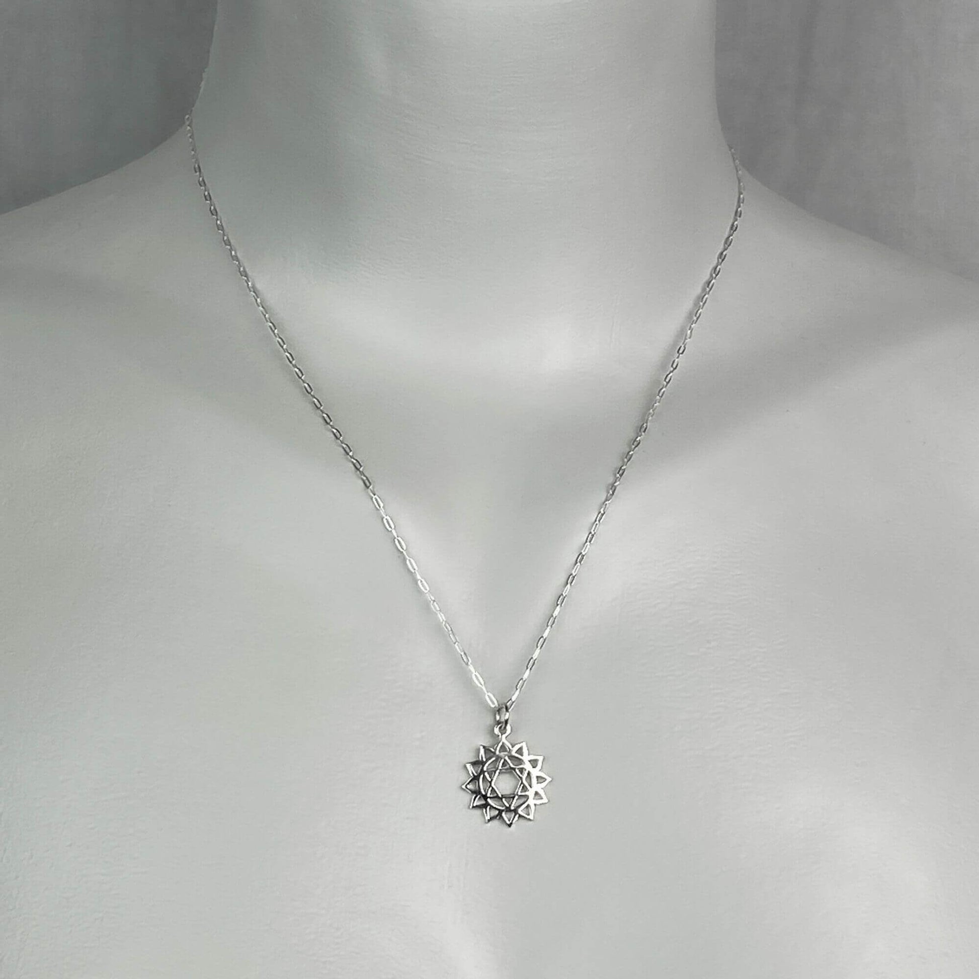 A woman model wearing a sterling silver chain necklace with a small silver heart chakra charm.