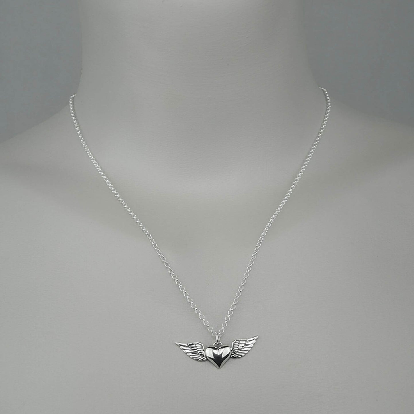 A woman wearing a sterling silver chain necklace with a trendy heart with wings  small charm.