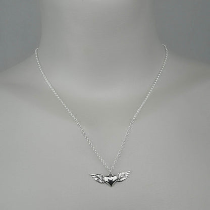 A woman wearing a sterling silver chain necklace with a trendy heart with wings  small charm.