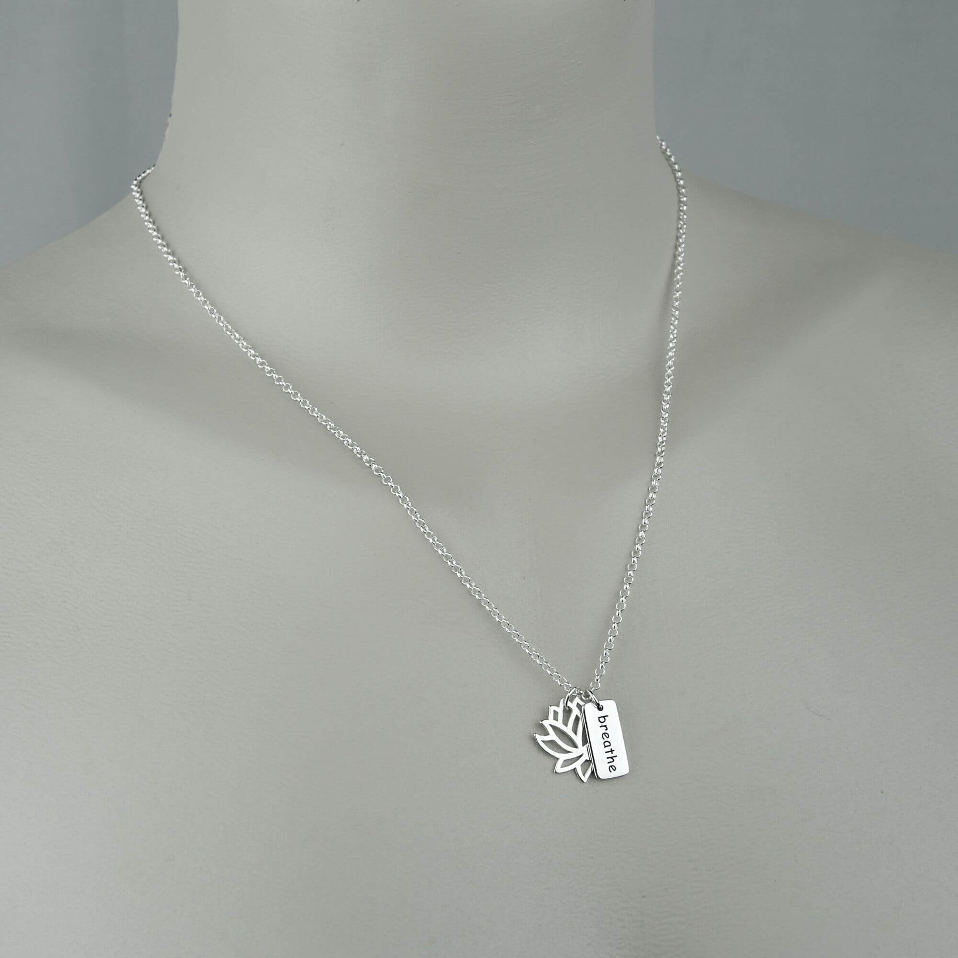 A woman wearing a sterling silver chain necklace with a trendy lotus charm necklace. Openwork lotus and breathe saying rectangle charms.