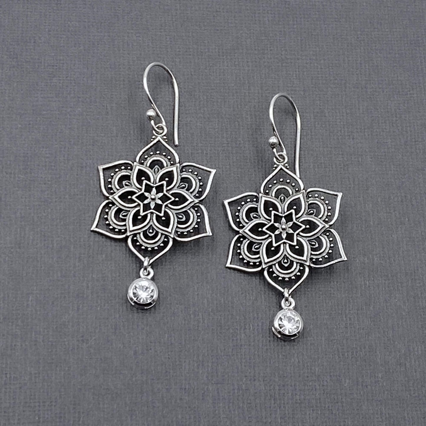 Detailed view of silver feminine earrings with a spiritually-inspired mandala design and small hanging crystal.