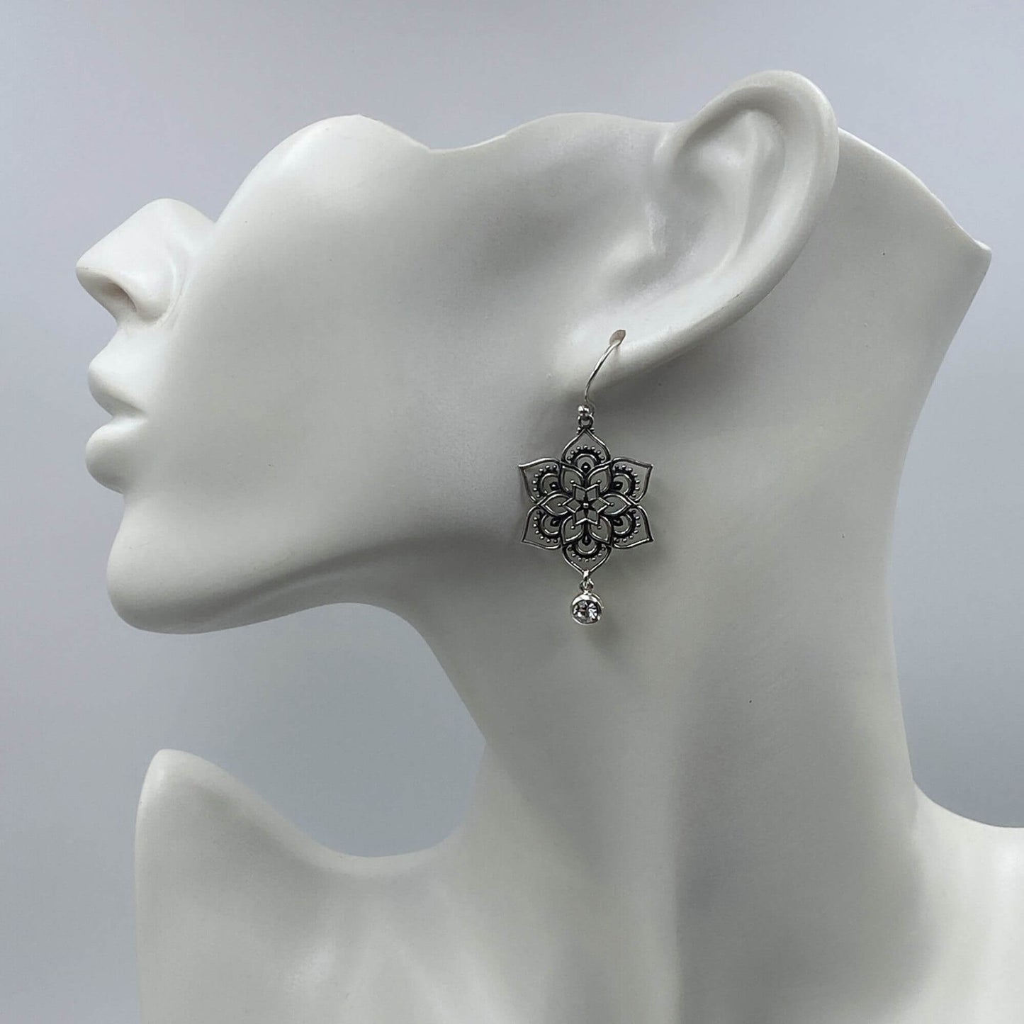 Model of a woman wearing large intricate sterling silver mandala dangle earrings.