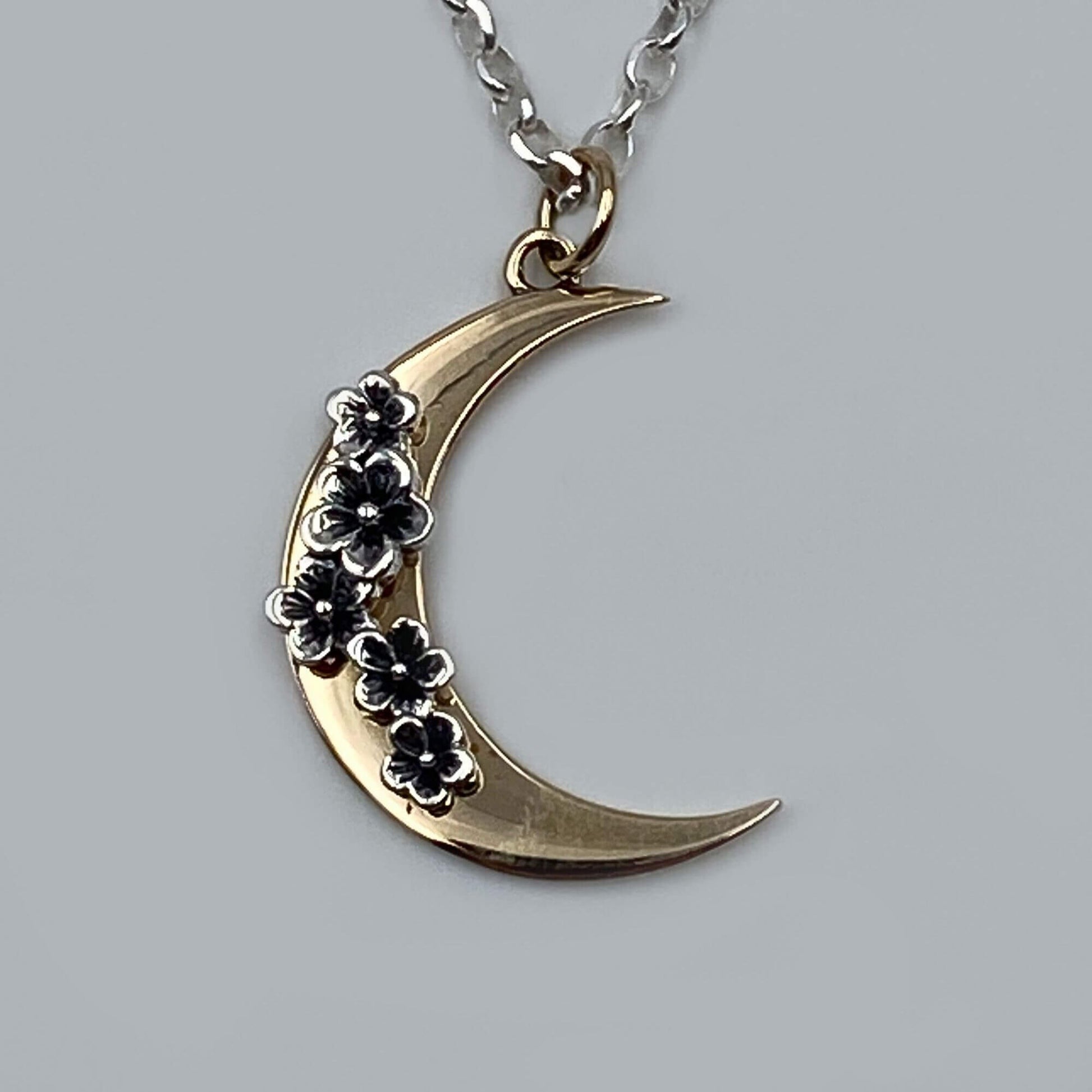 Detailed view of a gold crescent moon with five silver patina flowers pendant dangling from a chain.