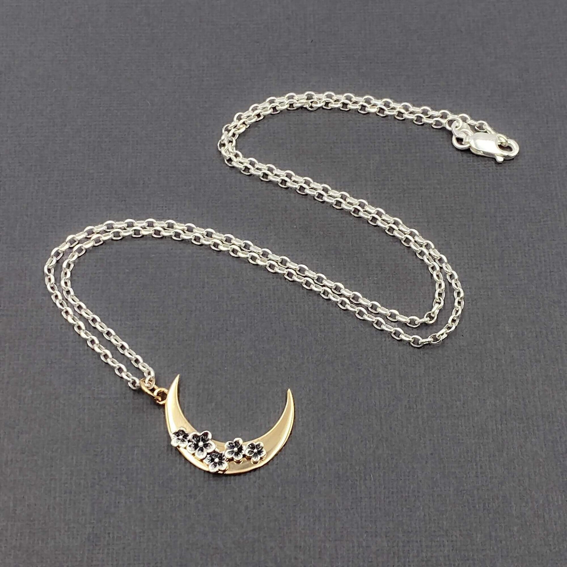 Detailed view of a crescent moon necklace that is shiny gold and silver with a silver chain.