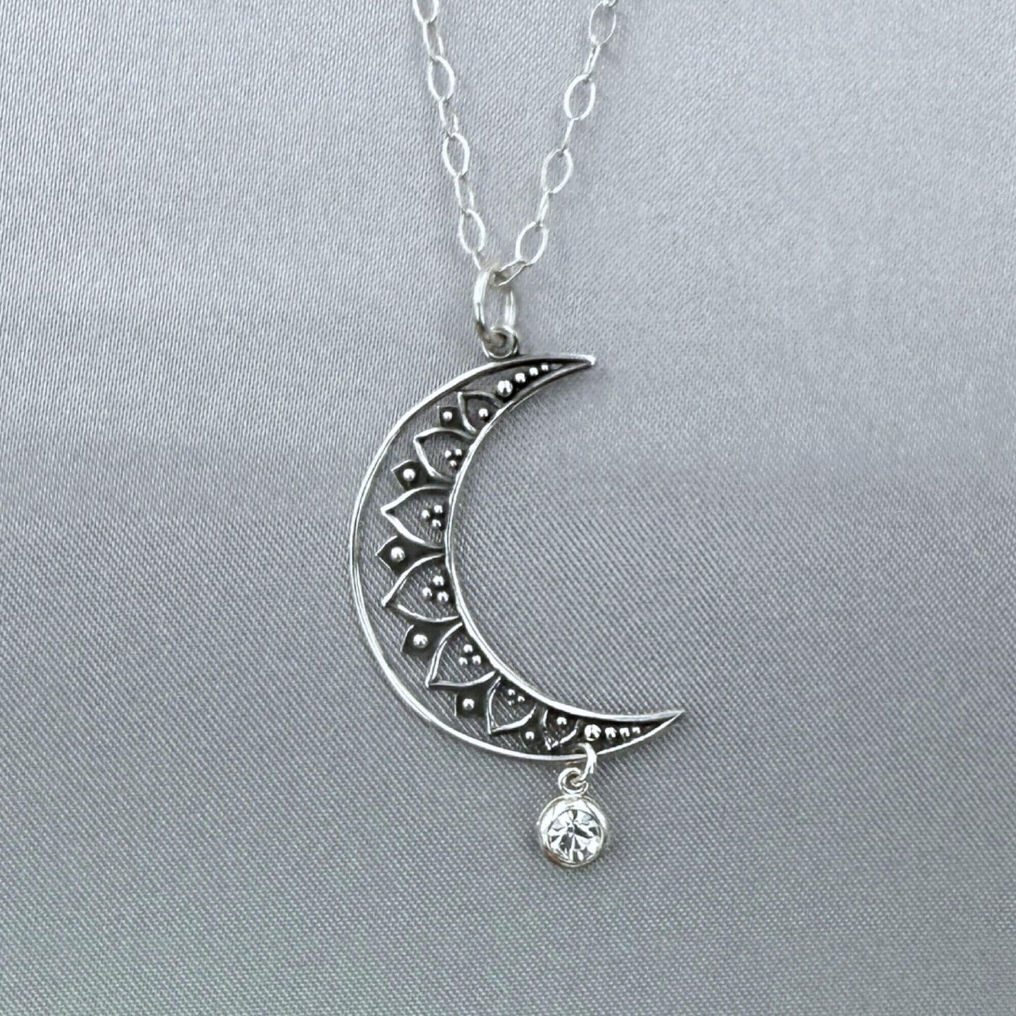 Close-up angle of silver moon and star pendant hanging from a sterling silver cable chain. The crescent moon is a filigree design and the crystal dangles freely at the bottom.