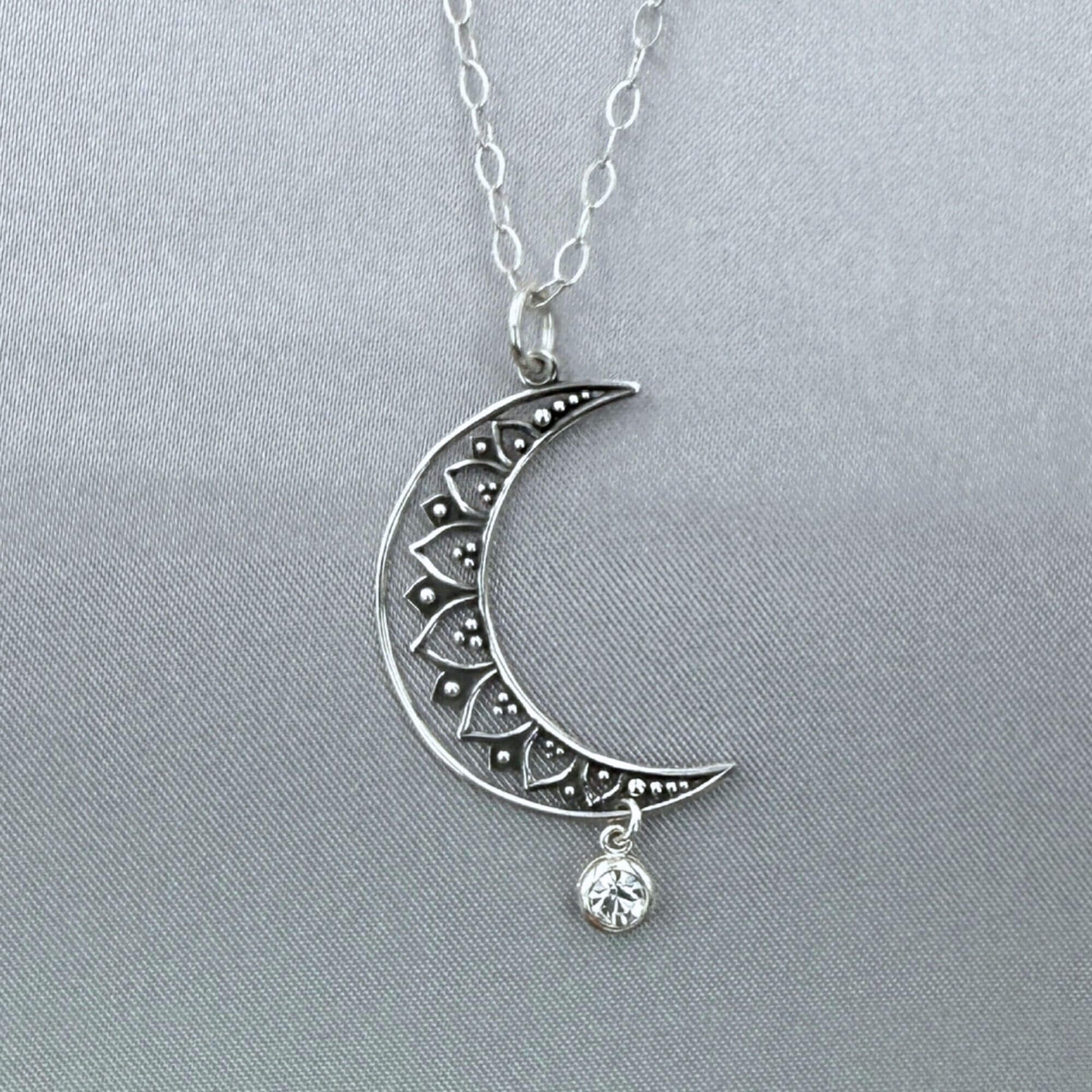 Close-up angle of silver moon and star pendant hanging from a sterling silver cable chain. The crescent moon is a filigree design and the crystal dangles freely at the bottom.