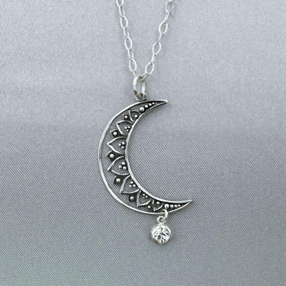 Close-up angle of silver moon and star pendant hanging from a sterling silver cable chain. The crescent moon is a filigree design and the crystal dangles freely at the bottom.