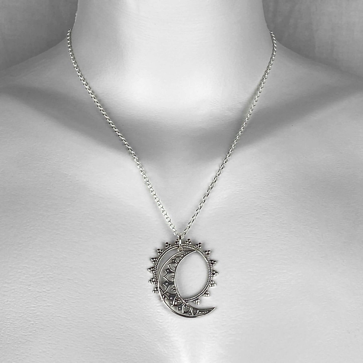 A woman wearing a sterling silver chain necklace with a celestial sun and moon dangling pendants.