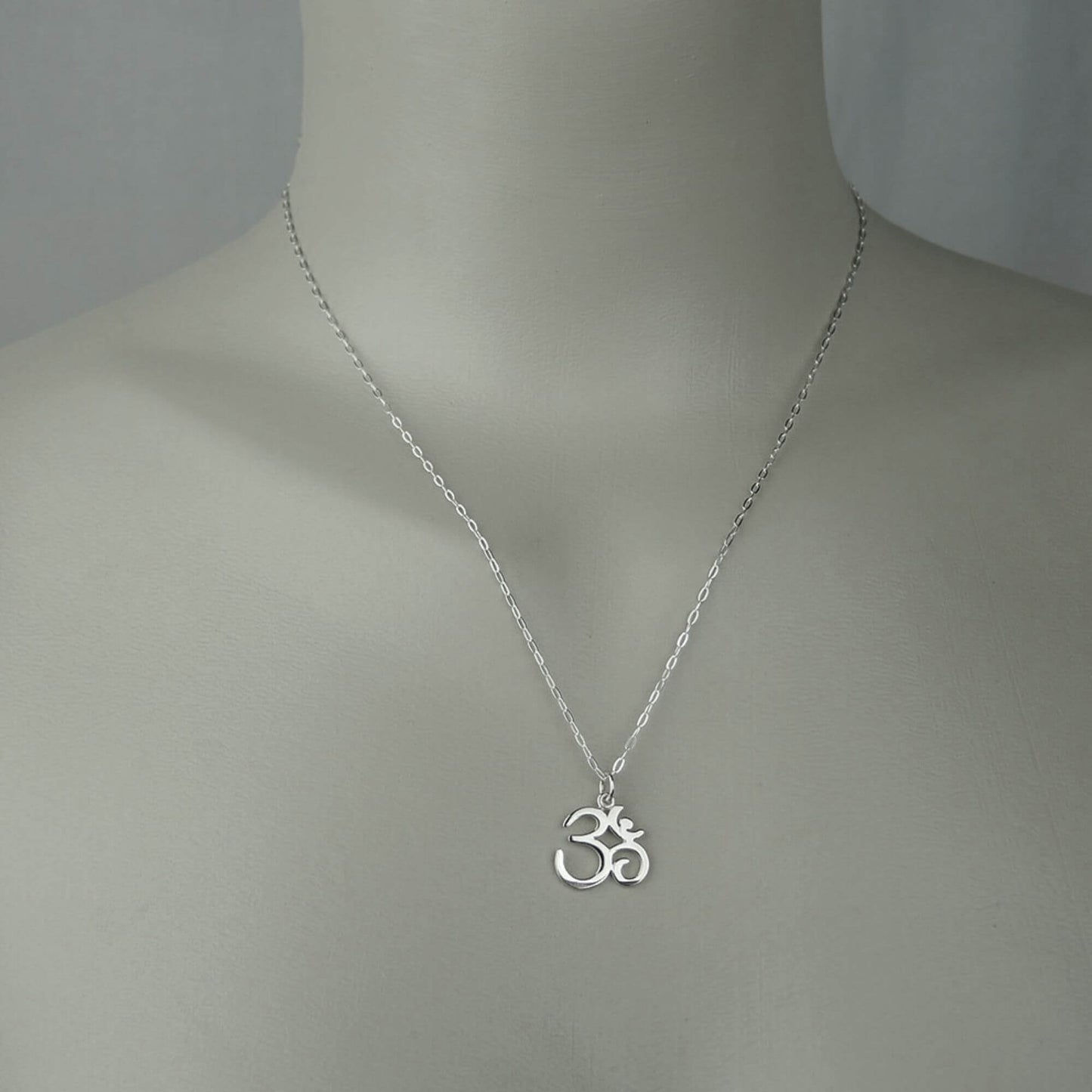 A woman wearing a sterling silver chain necklace with a small ohm or om symbol script on a dainty small charm.