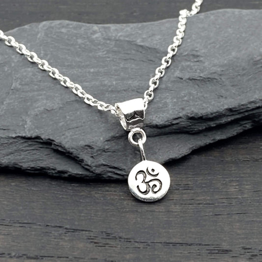 Tiny round Ohm charm dangling off a silver modern bail with a sterling silver cable chain necklace.