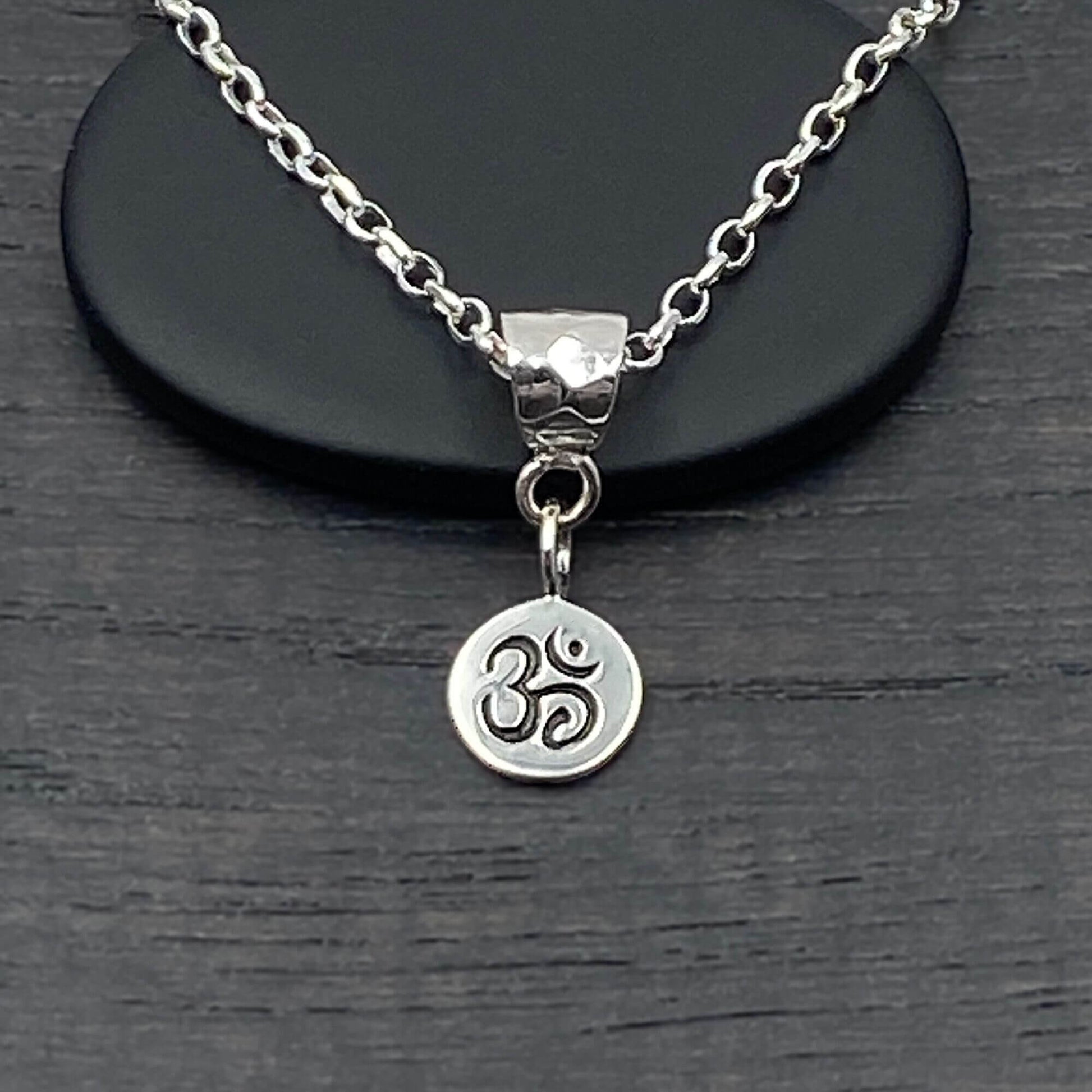 Detailed view of a handmade small Ohm Om charm that is etched with the Om symbol in a darker patina. 