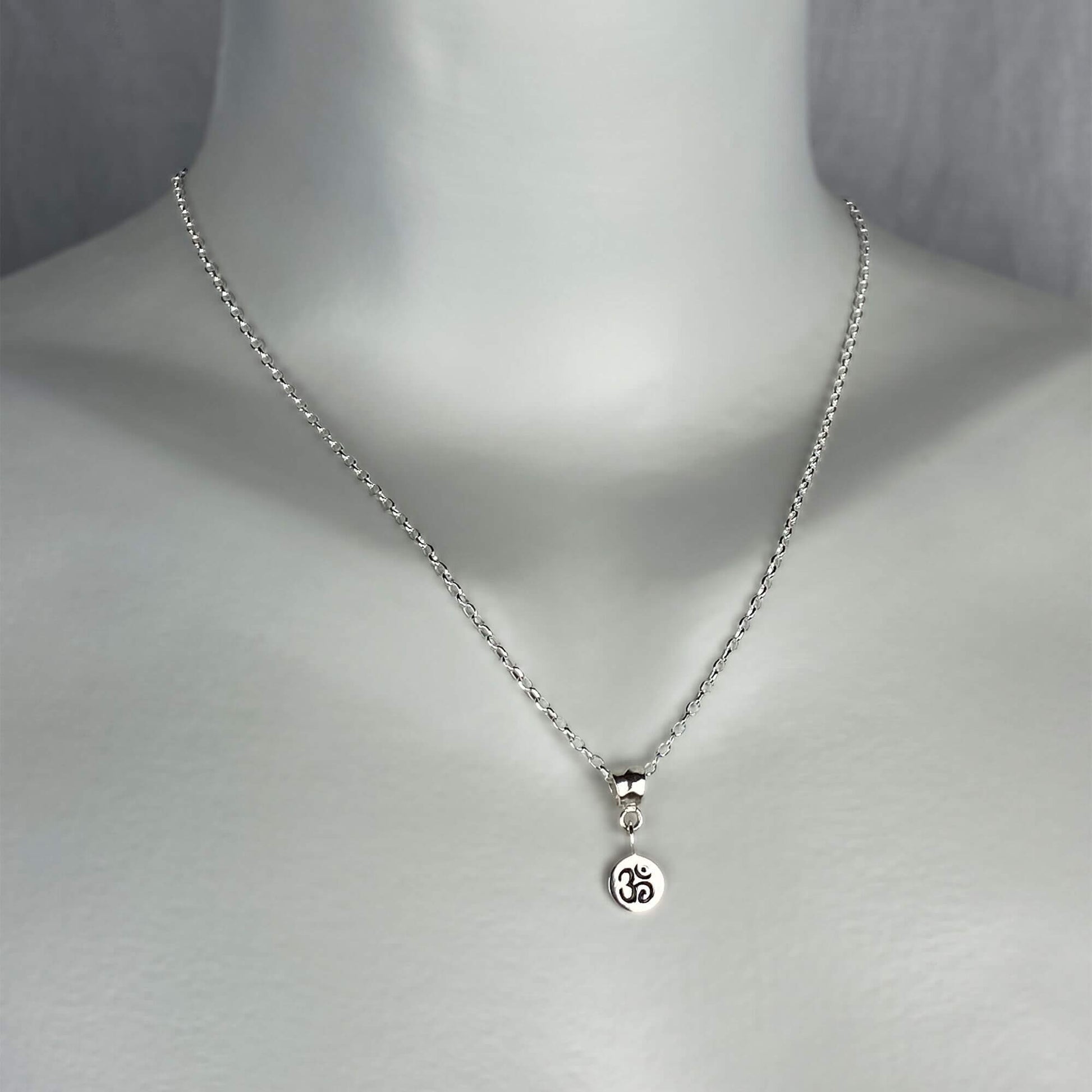 A woman model wearing a sterling silver chain necklace with a trendy small ohm charm dangle. yoga jewelry.