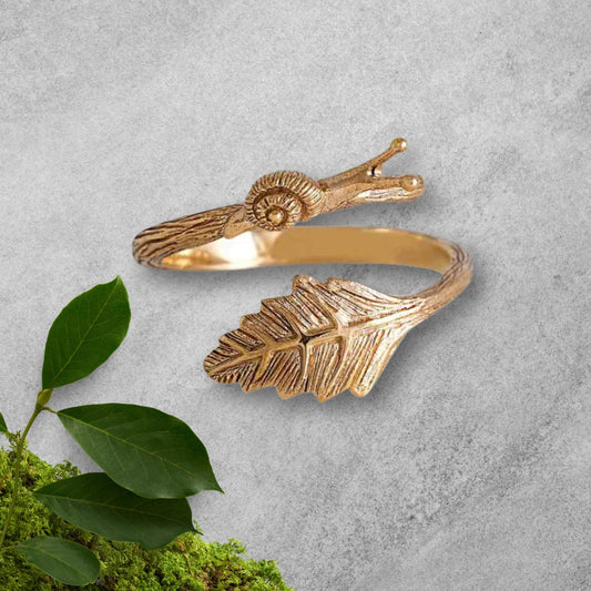 Close up of the cutest solid gold bronze adjustable snail ring for women.  The gold band is detailed like bark and wraps around the front ending in a highly detailed snail and other side a detailed leaf. 