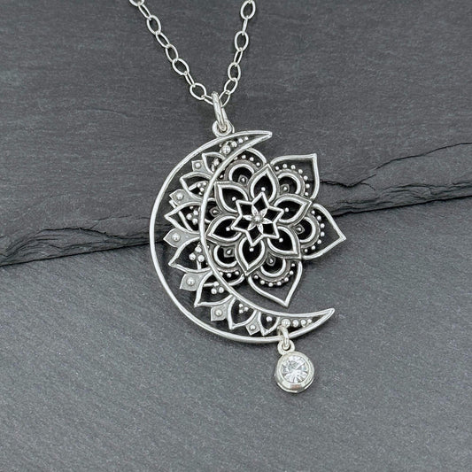 CLose up view of a 925 sterling silver sun, moon and star pendant necklace for women.  The crescent moon and sun are cut out with intricate filigree shapes in the bali style.  There is a crystal dangle hanging off the bottom of the moon.