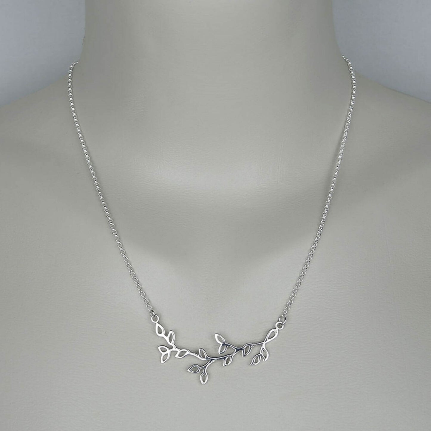 A woman wearing a sterling silver chain necklace with a trendy tree branch with leaves  pendant.