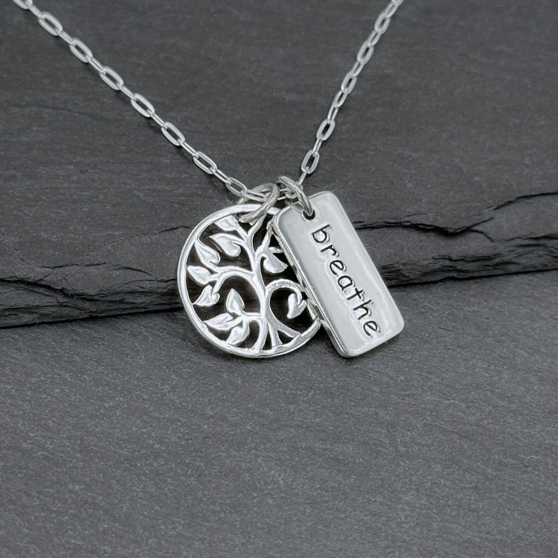 Close-up view of a 925 solid sterling silver charm necklace with two small charms: a round tree of life with an openwork cutout design about 5/8" tall, and a small rectangle charm with the word Breathe etched on it.  The two small charms dangle freely of one another—perfect gift for yoga lovers.