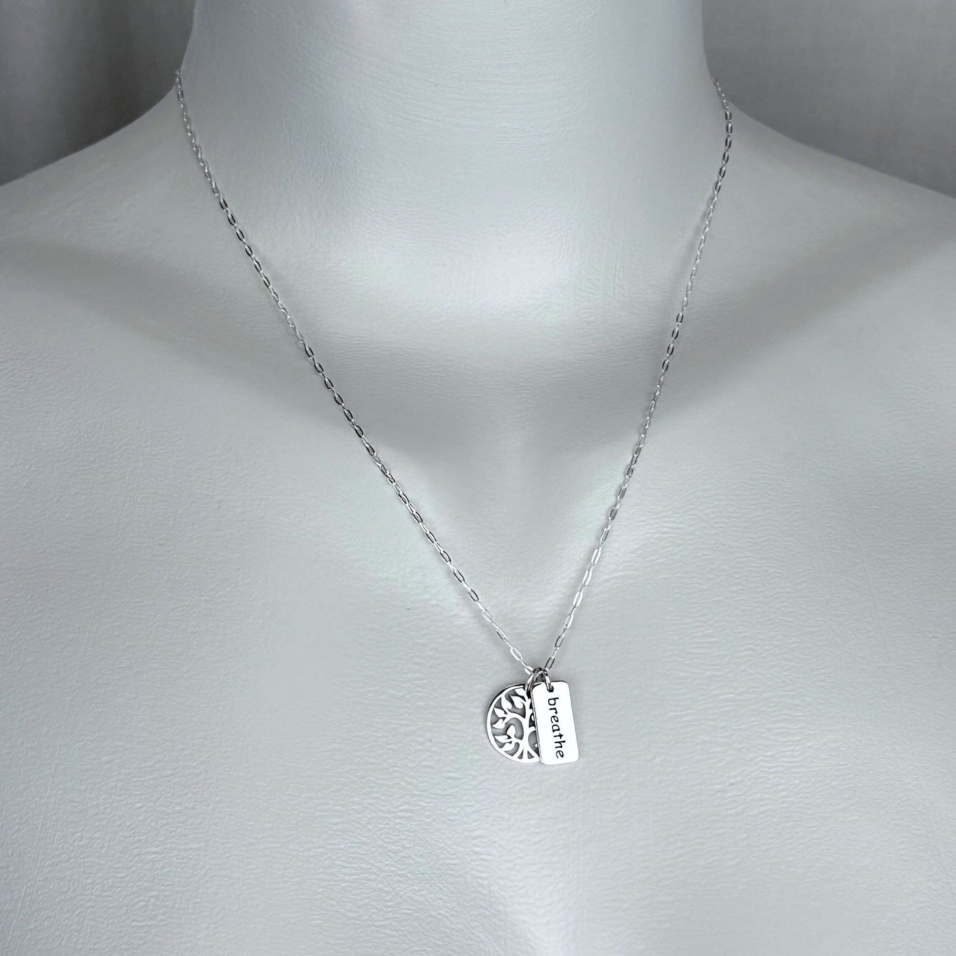 A woman wearing a 925 solid sterling silver necklace with a double charm of a tree and a breathe word pendant with a 925 solid sterling silver chain. Our silver jewelry collection is intended for females.