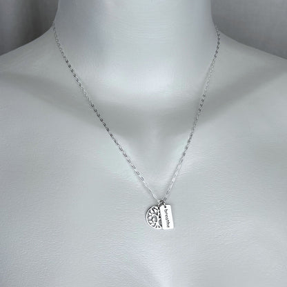 A woman wearing a 925 solid sterling silver necklace with a double charm of a tree and a breathe word pendant with a 925 solid sterling silver chain. Our silver jewelry collection is intended for females.